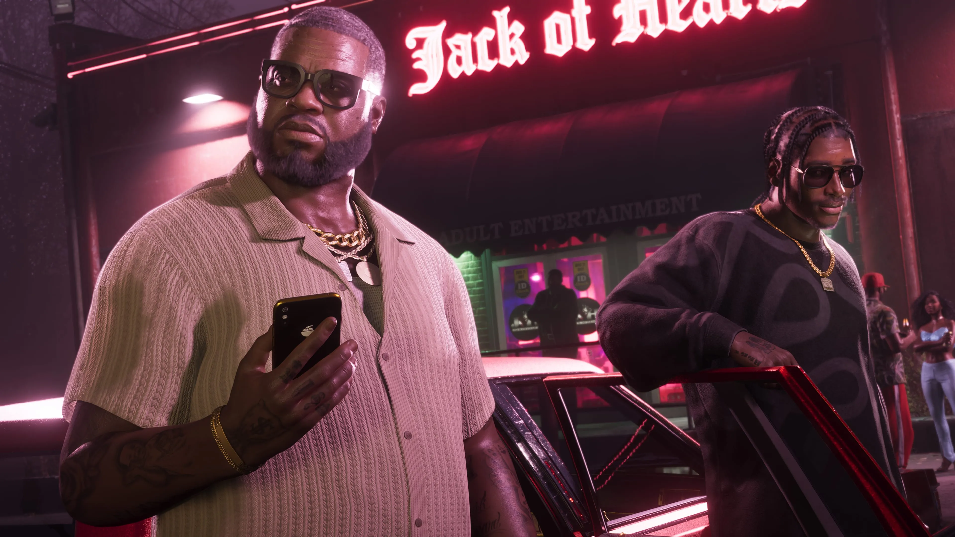 Boobie Ike standing with a phone in his hand outside the neon-lit Jack of Hearts club in GTA 6, as another man in sunglasses steps out of a red car beside him. Official Rockstar Games screenshot.