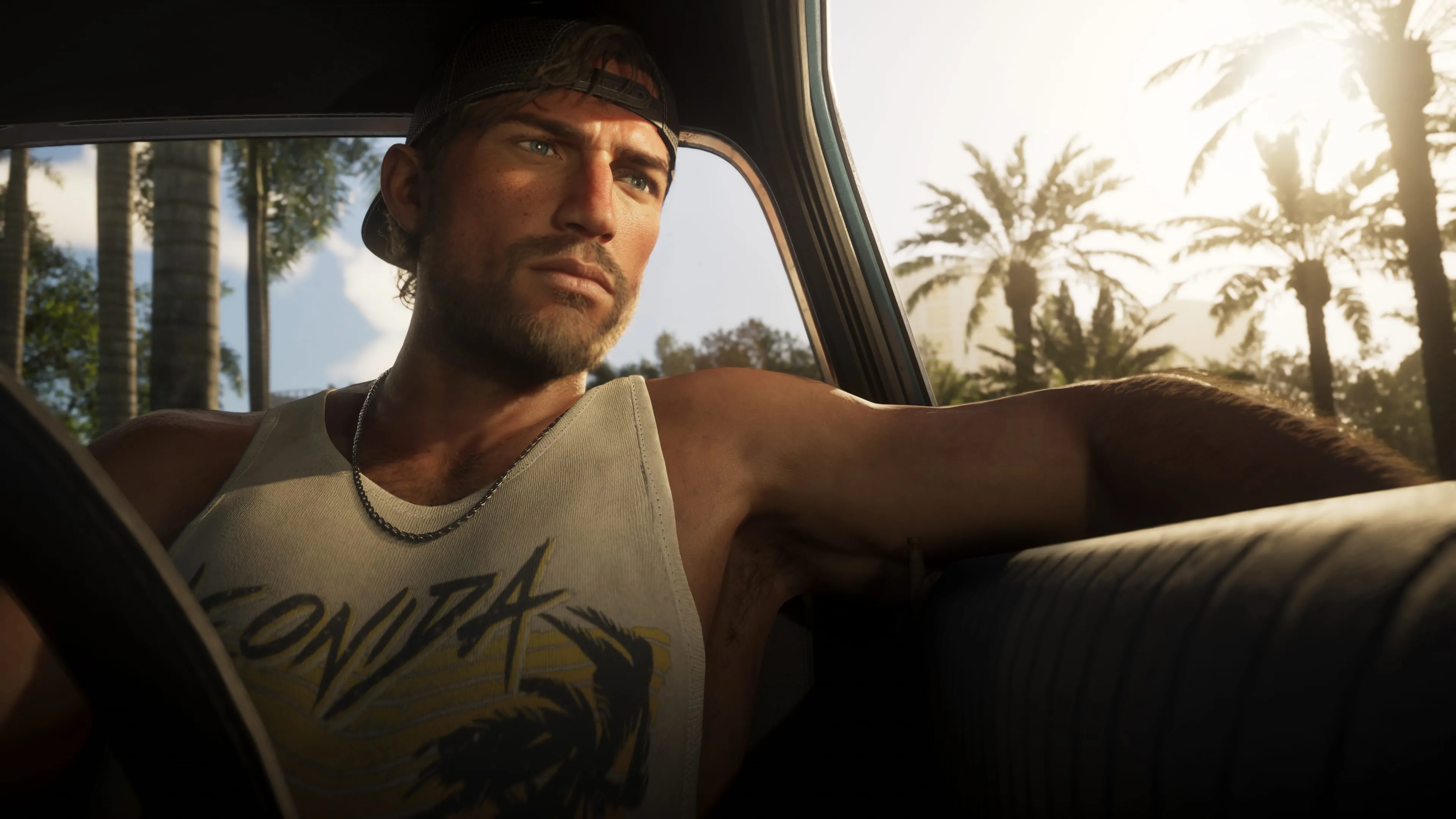 Jason Duval at the wheel of a car in GTA 6, wearing a backwards cap and a Leonida tank top, with sunlit palm trees through the window. Official Rockstar Games screenshot.