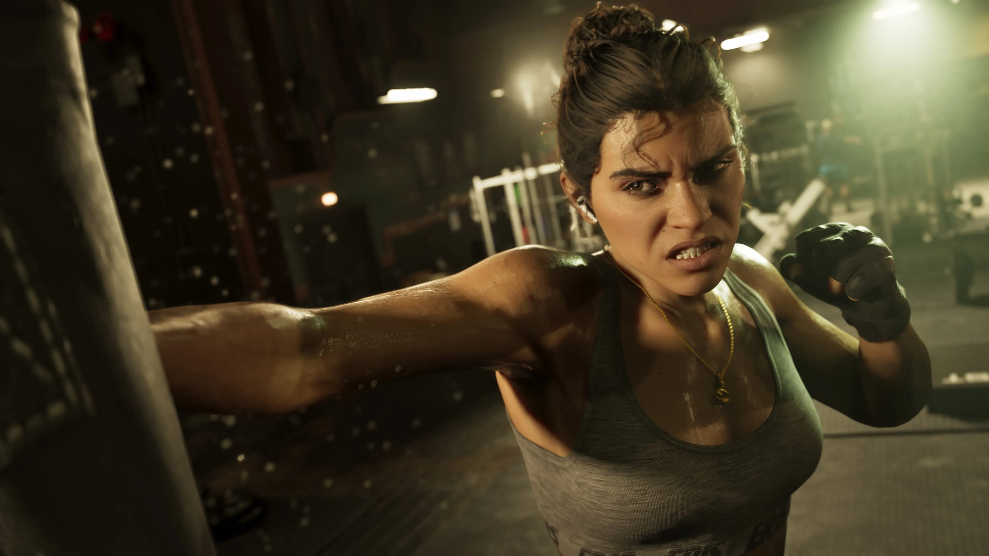 Lucia Caminos throwing a punch at a heavy bag in a dimly lit gym in GTA 6, wearing a grey training top and a fingerless glove. Official Rockstar Games screenshot.