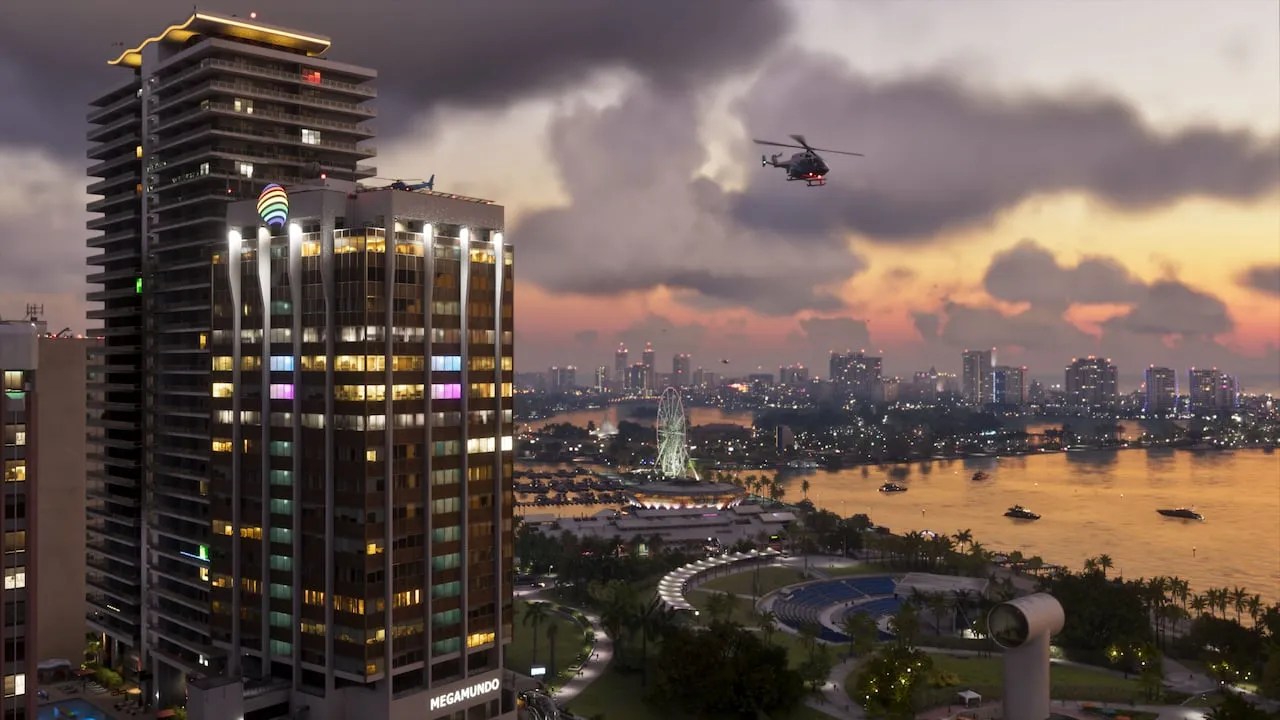 A Vice City high-rise with the MEGAMUNDO sign at dusk in GTA 6, with a helicopter overhead and a Ferris wheel on the bay behind it. Official Rockstar Games screenshot.